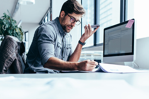 Man sat at a desk, speaking on the phone as he looks at his notepad