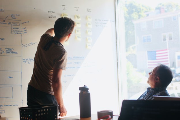 Two males in an interactive meeting, using a whiteboard and post-it notes for ideas