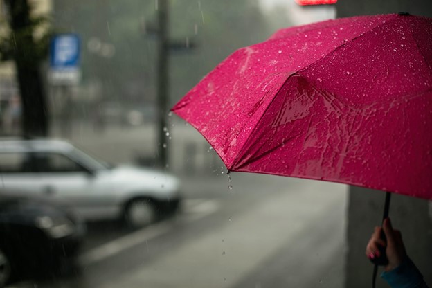 Person holding red umbrella on the side of the street in the rain