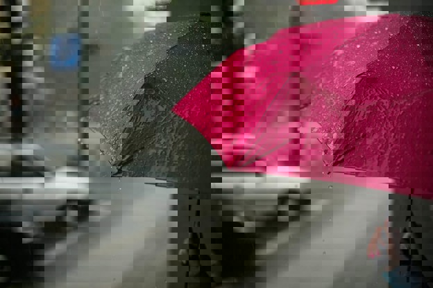 Person holding red umbrella on the side of the street in the rain