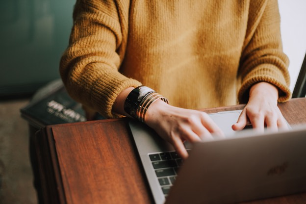 Person in a yellow jumper sat typing on a laptop